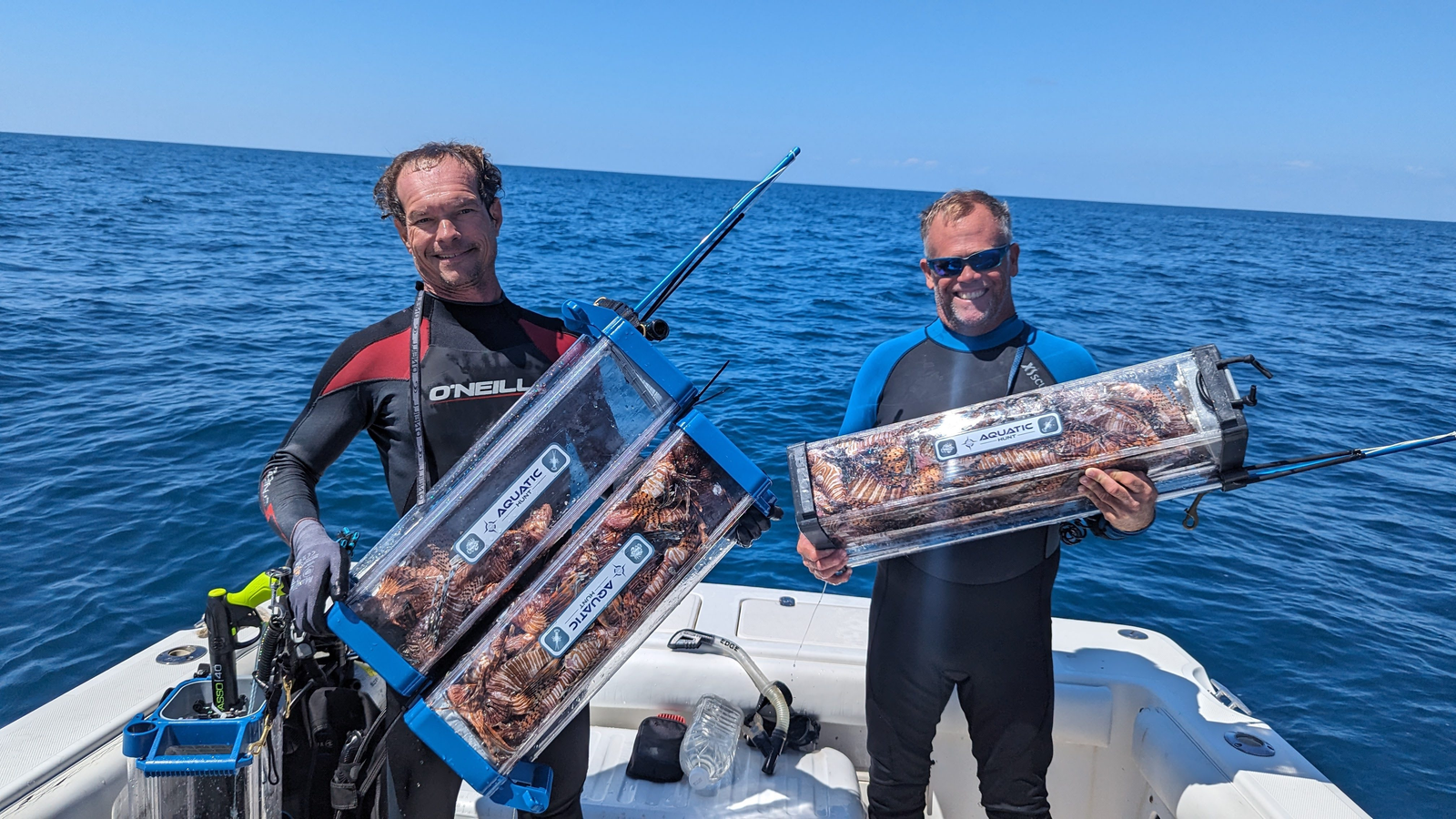 Two divers on a boat holding tubes packed with culled lionfish