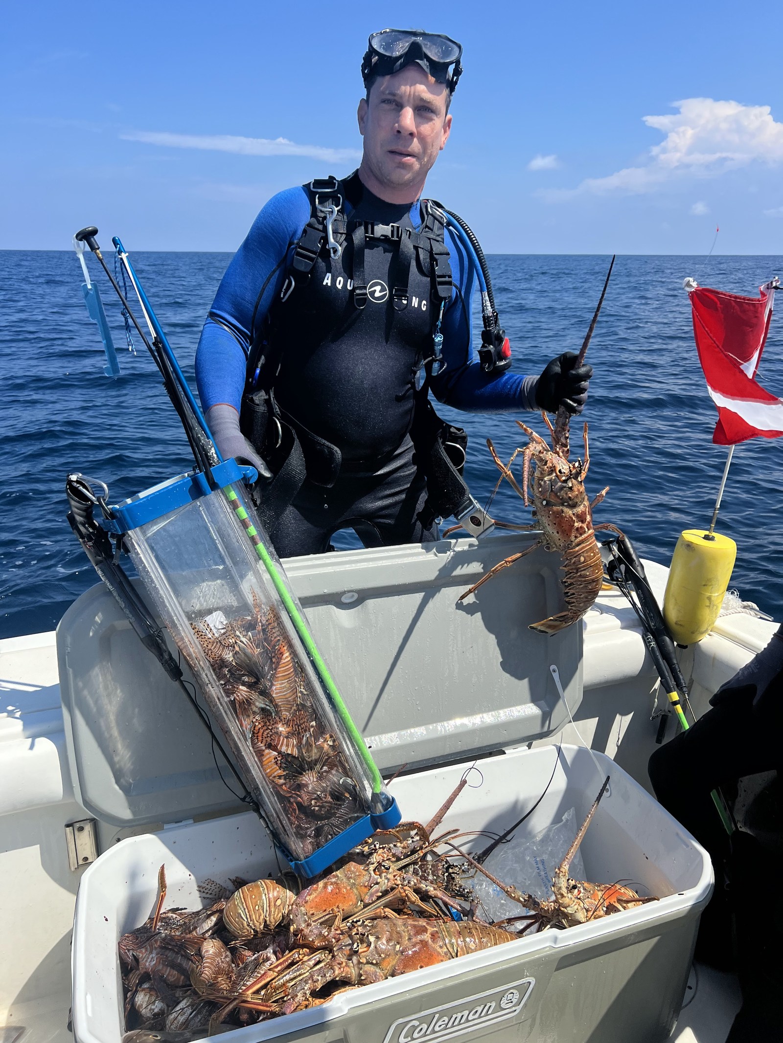 Diver on a boat with lobsters and a cooler full of lionfish